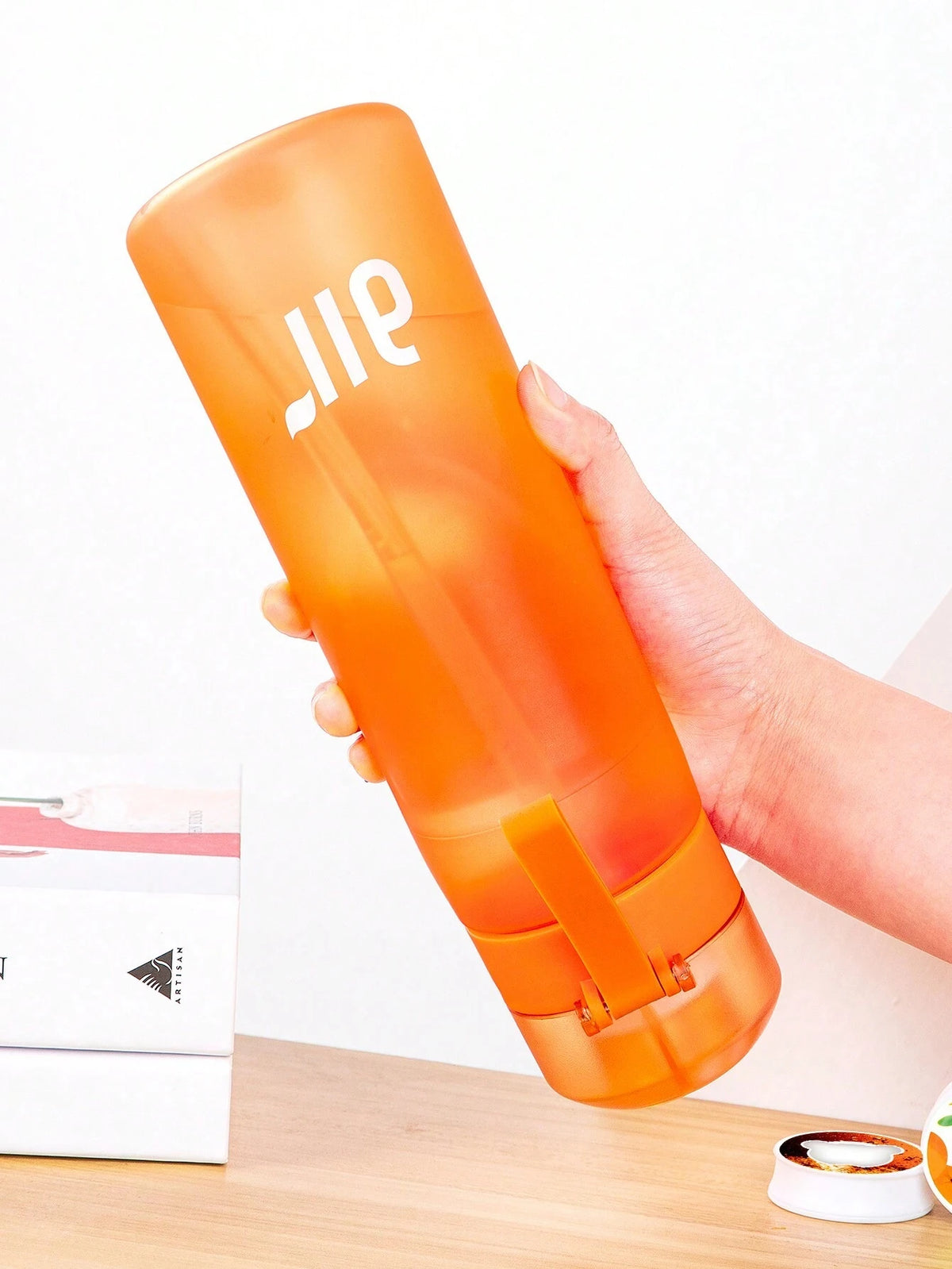 Orange air water bottle held tilted; translucent body with flip top lid