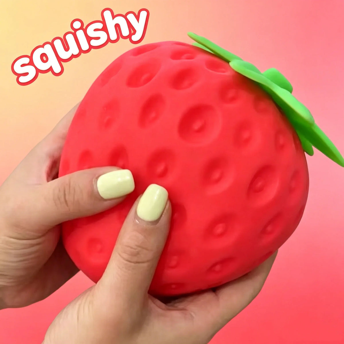 Close-up red strawberry squishy toy with green leaves, held by hands with pale nails.