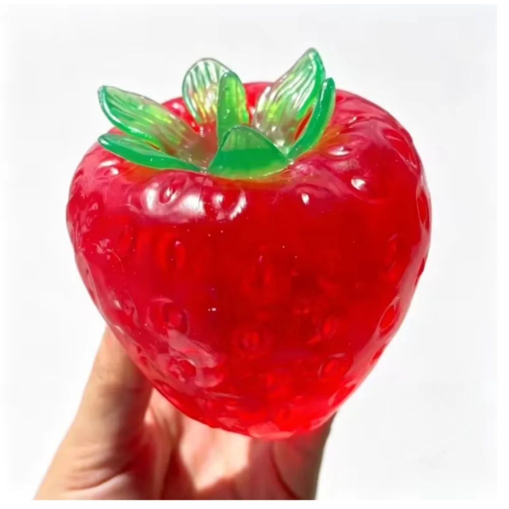 Red strawberry squishy stress ball with green leaves, held in a hand
