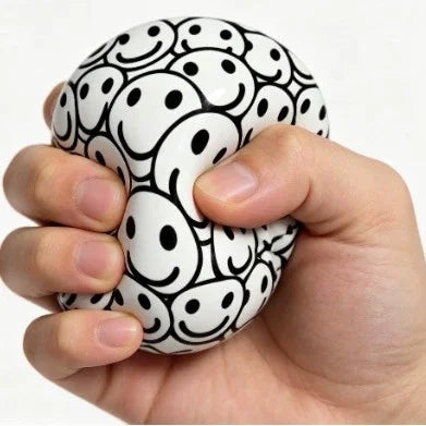 Round stress ball with white base and black doodle faces, held in hands