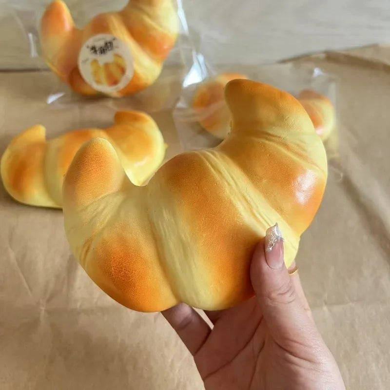 Golden-yellow croissant-shaped squishy toy, held in hand against package