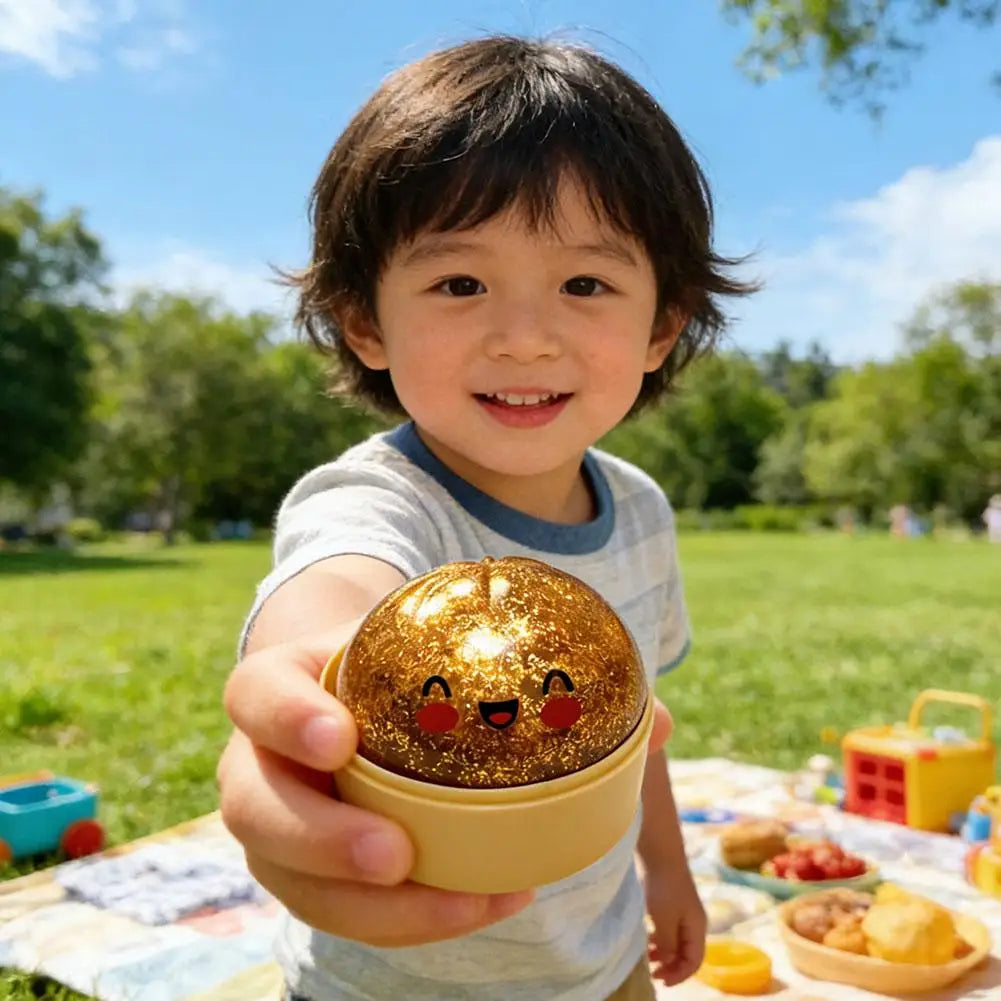 Golden bun-shaped squishy stress ball with smiling face, held in child’s hand