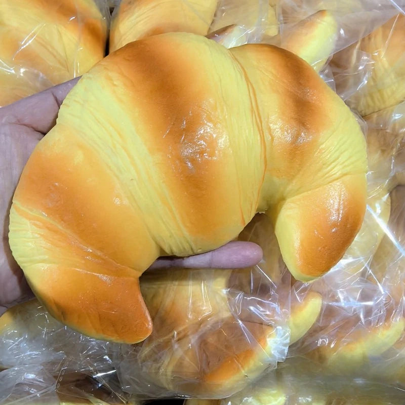 Squishy croissant-shaped stress relief toy, glossy yellow-orange, held in hand