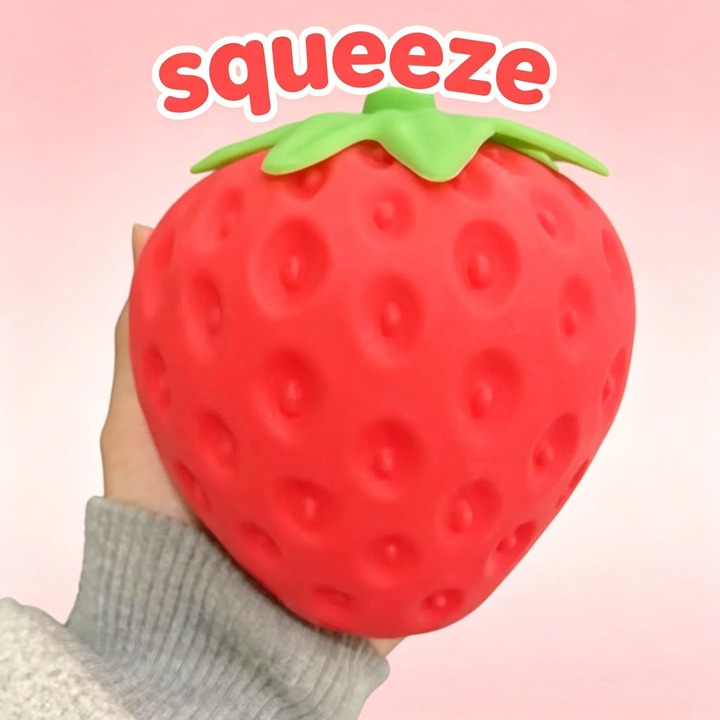 Red strawberry squishy stress ball with green top leaves, held upright; bumpy surface