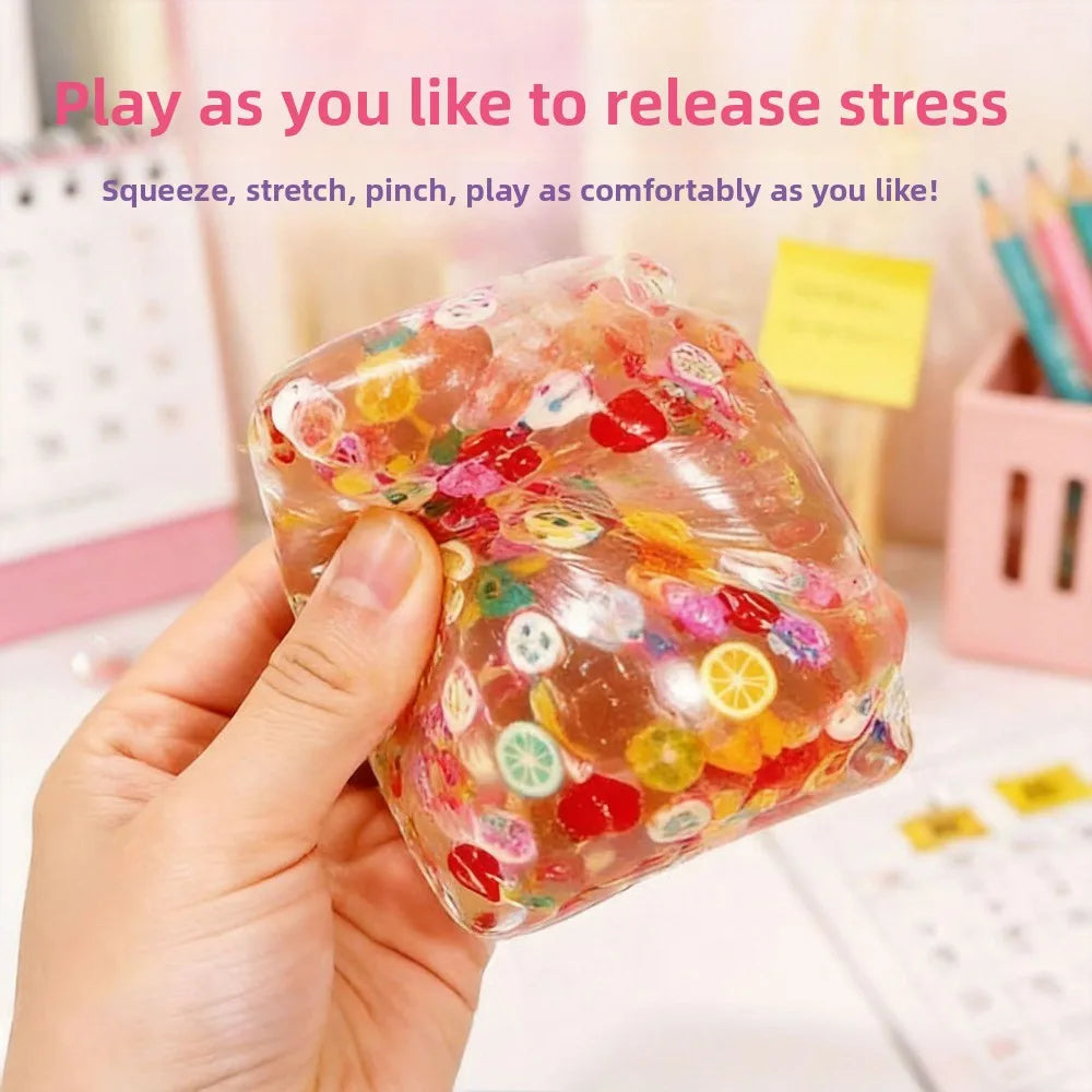 Hand holding clear fruit-themed squishy cube stress ball with multicolor shapes