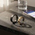 Black and gold smart health rings resting on a countertop with sensor windows visible